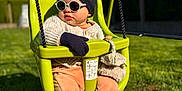 Jules participe au concours pour gagner de l'argent avec cette photo : baby, swing, hat, glasses, outdoor, grass, child, sunny, gloves, knitwear, playground, seat, green, blue_sky, pants, cute, toddler, sunshine, relaxing, park