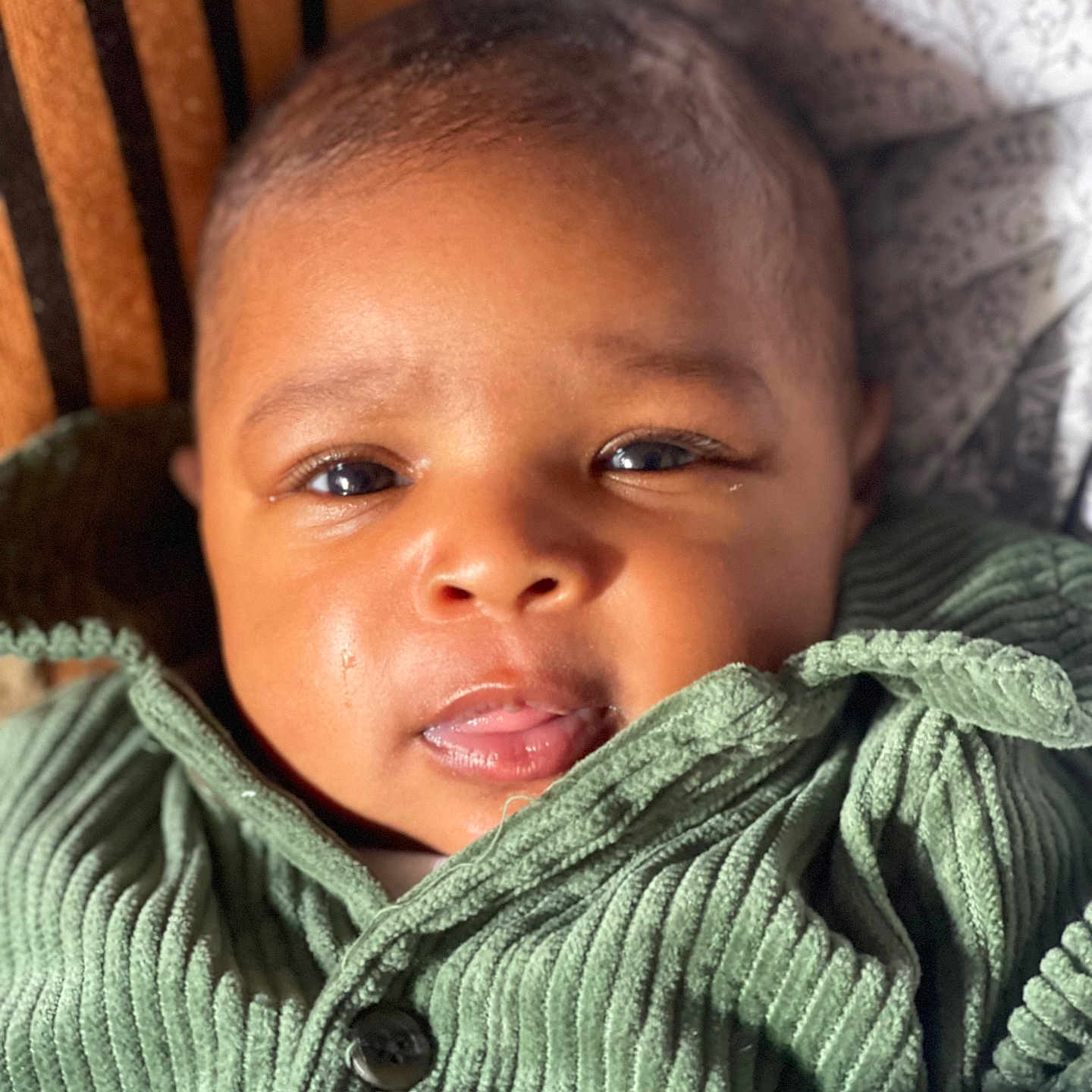 Zarah a rejoint le concours — aidez-le/la à gagner de superbes lots ! baby, closeup, clothing, cozy, cute, expression, eyes, face, green_jacket, hand, indoor, infant, mouth, patterned_background, portrait, ribbed_fabric, skin, soft_texture, warm_lighting, young_child