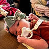 baby, infant, child, portrait, lying_down, couch, pacifier, bow, headband, red_clothing, blanket, indoor, home, cozy, smiling, face, eyes, hands, soft_lighting, close_up