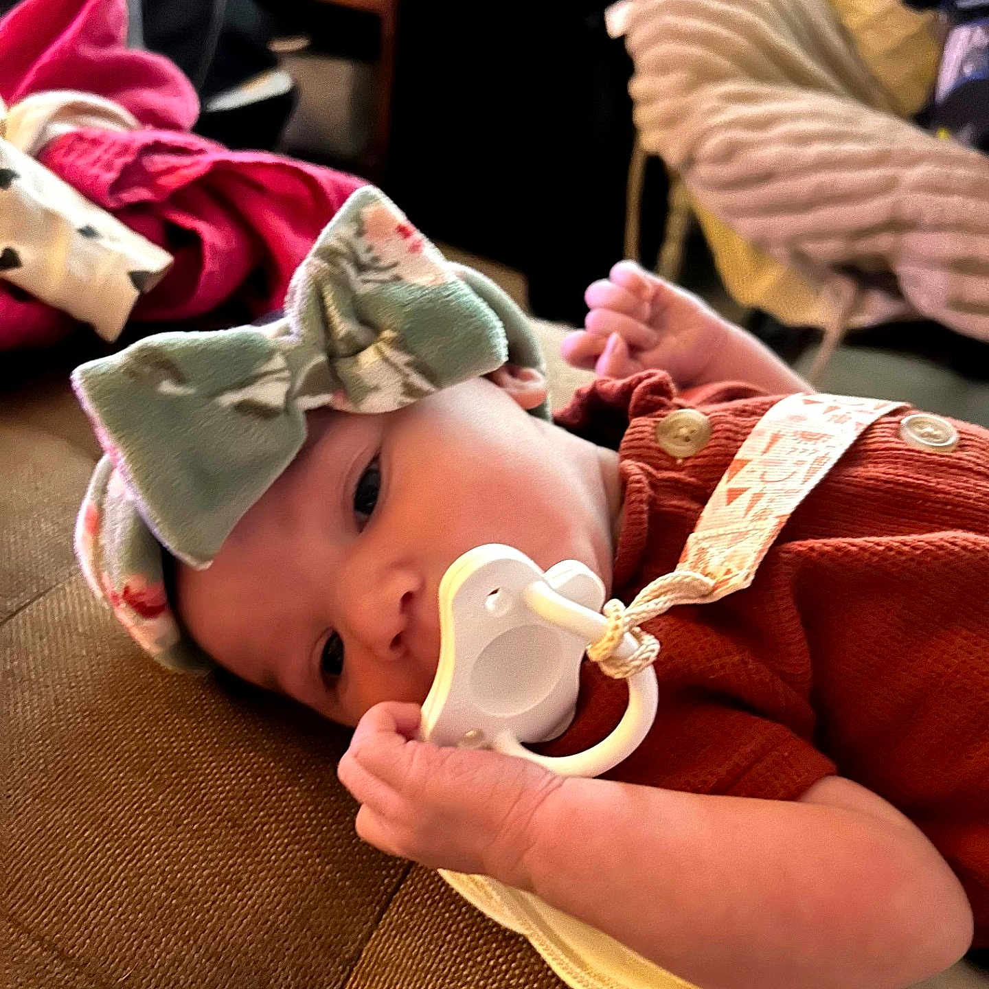 Aedrah is registered to the contest to win money with this photo: baby, infant, child, portrait, lying_down, couch, pacifier, bow, headband, red_clothing, blanket, indoor, home, cozy, smiling, face, eyes, hands, soft_lighting, close_up