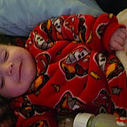 Rj Thomas is registered to the contest to win money with this photo: baby, sleeping, red_clothing, blanket, bottle, cartoon_pattern, cozy, infant, bedtime, soft_texture, hand, face, closed_eyes, comfort, rest, child, indoors, cuteness, warmth, pajamas