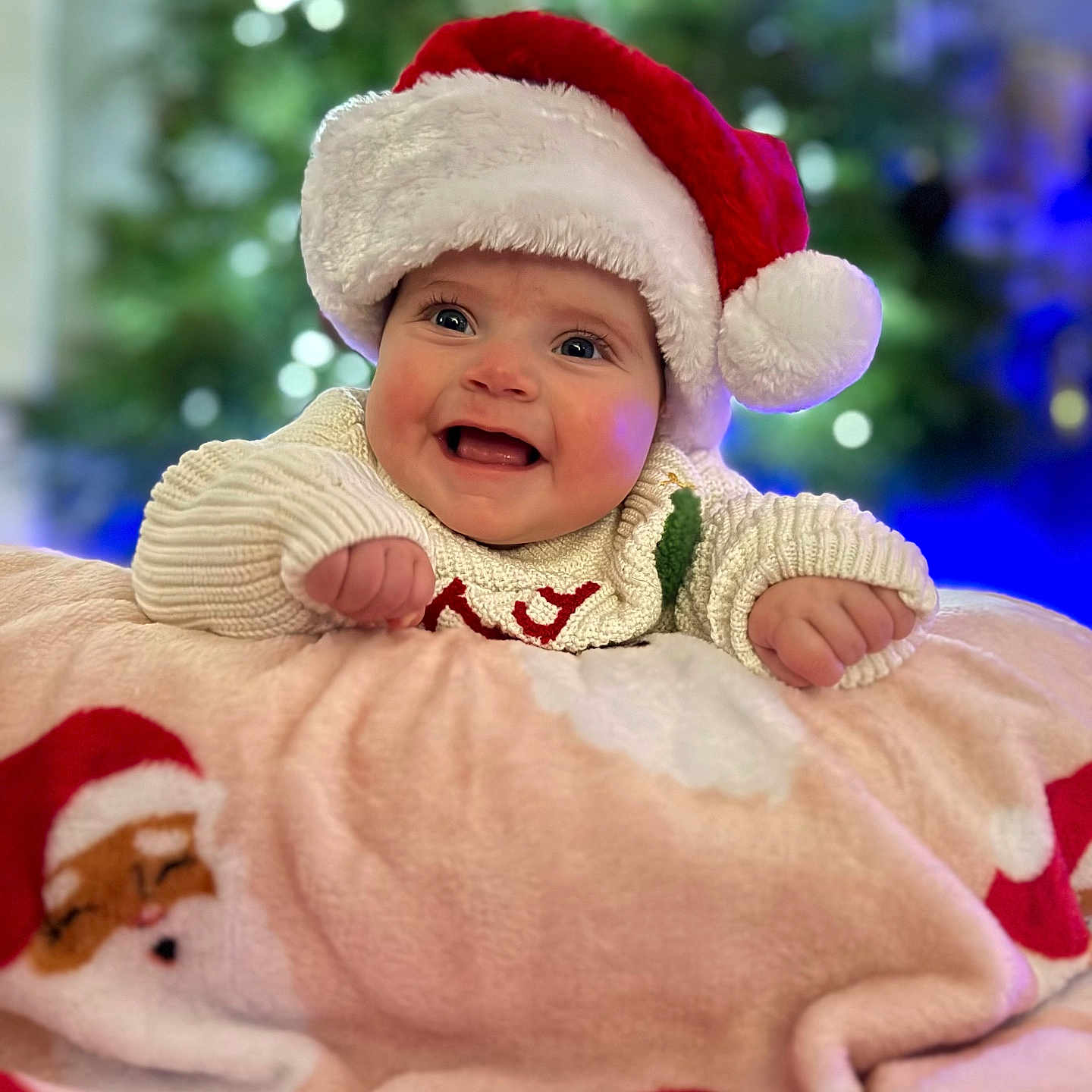 Remi is registered to the contest to win money with this photo: baby, blanket, celebration, child, christmas, christmas_tree, cozy, cute, decoration, face, festive, happy, holiday, indoors, infant, portrait, santa_hat, smiling, sweater, warm