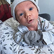 Tayvin is registered to the contest to win money with this photo: baby, bedding, blanket, blue_eyes, close_up, cute, expression, face, hat, headwear, indoor, infant, leaf_pattern, lying_down, mittens, newborn, onesie, pillow, portrait, soft_lighting