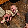 baby, bottle, cabinet, child, crawling, cute, flooring, floral_dress, foot, hand, happy, home, indoor, infant, person, rug, smartphone, smiling, syringe, wooden_floor