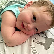 Paisley is registered to the contest to win money with this photo: baby, smiling, face, blanket, pillow, child, cute, infant, lying_down, happy, cheeks, blue_eyes, hair, sleeping_area, cozy, soft, indoors, clothing, pattern, resting