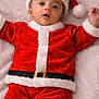 baby, belly, blanket, child, christmas_outfit, cute, face, festive, happy, headwear, holiday, indoor, infant, lying_down, portrait, red_clothing, santa_hat, smiling, soft_texture, white_fur_trim