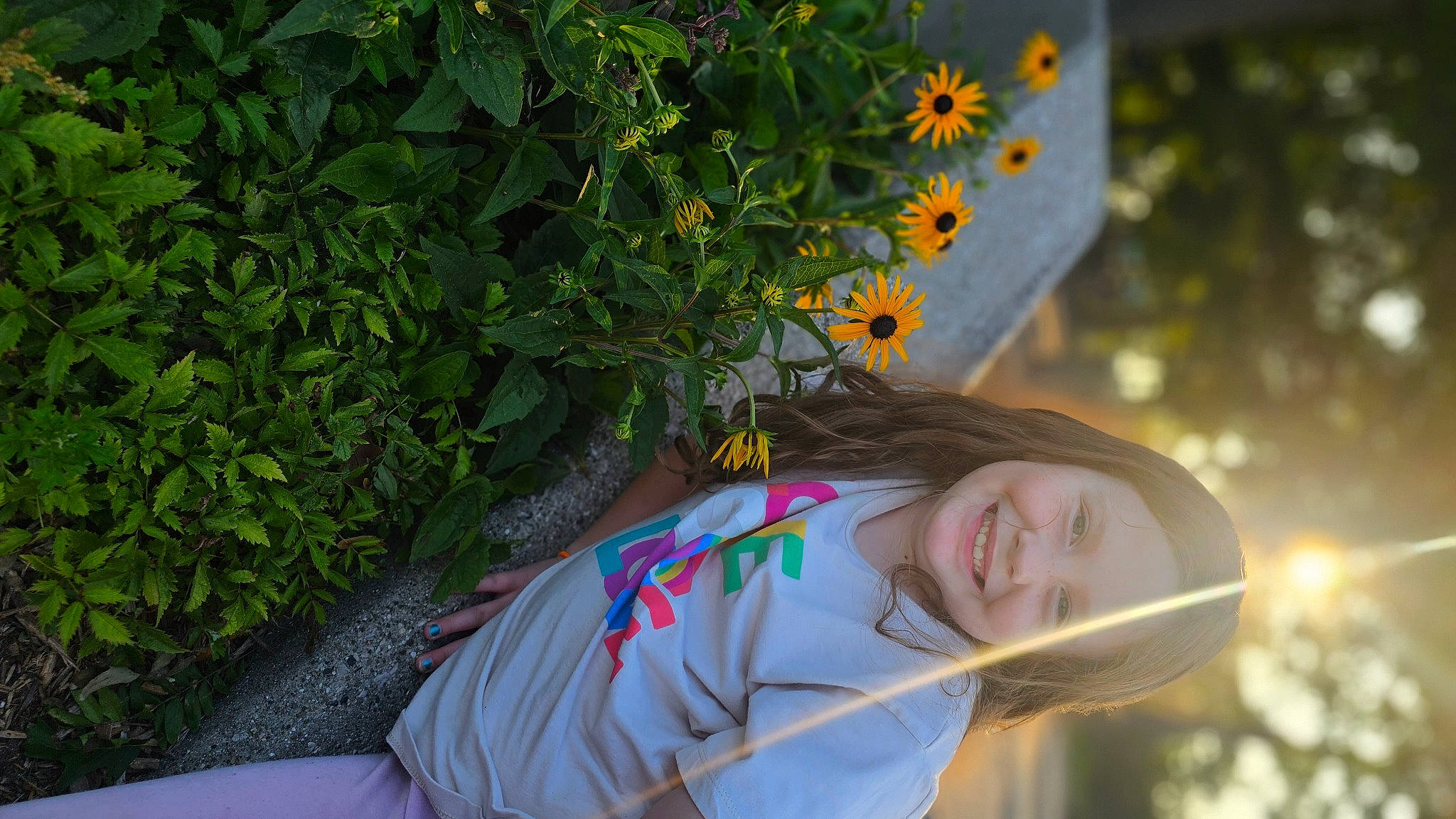 Krista is registered to the contest to win money with this photo: annual_plant, brown_hair, electric_blue, flower, flowering_plant, fun, garden, grass, happy, joy, leisure, people_in_nature, person, plant, portrait_photography, shrub, sitting, smile, sunflower, t_shirt
