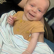 Bennett is registered to the contest to win money with this photo: baby, smiling, blanket, shirt, infant, person, arm, hand, portrait, cute, happy, human, child, clothing, skin, face, holding, casual, indoor, closeup