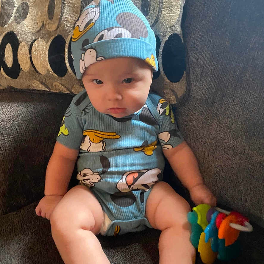 Jordan is registered to the contest to win money with this photo: baby, beanie, bodypart, bonnet, cap, clothing, couch, face, finger, furniture, hand, hat, head, newborn, pants, person, photography, portrait, shorts, sitting
