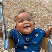 Zyon joined the competition — help win amazing prizes! baby, child, swing, playground, smiling, happy, outdoor, clothing, seat, metal, woodchips, person, cute, fun, joyful, toddler, face, holding, blue_shirt, brown_pants