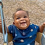baby, child, swing, playground, smiling, happy, outdoor, clothing, seat, metal, woodchips, person, cute, fun, joyful, toddler, face, holding, blue_shirt, brown_pants