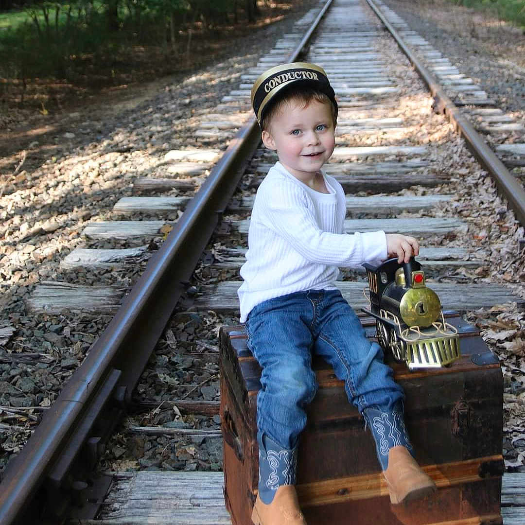 Jaxsyn is registered to the contest to win money with this photo: boy, child, clothing, face, footwear, head, jeans, male, pants, person, photography, plant, portrait, railway, shoe, sitting, soil, tree, vegetation, wood