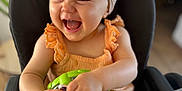 Nina a rejoint le concours — aidez-le/la à gagner de superbes lots ! baby, child, high_chair, headband, toy, laughing, happy, indoor, orange_clothing, ruffles, infant, person, seated, playful, cute, smiling, closeup, face, hands, furniture