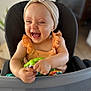 baby, child, high_chair, headband, toy, laughing, happy, indoor, orange_clothing, ruffles, infant, person, seated, playful, cute, smiling, closeup, face, hands, furniture