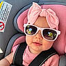 baby, child, infant, car_seat, sunglasses, pink_bow, pink_clothing, harness, portrait, sitting, face, smiling, outdoor, automobile, safety_belt, fashion, headband, close_up, photography, cute