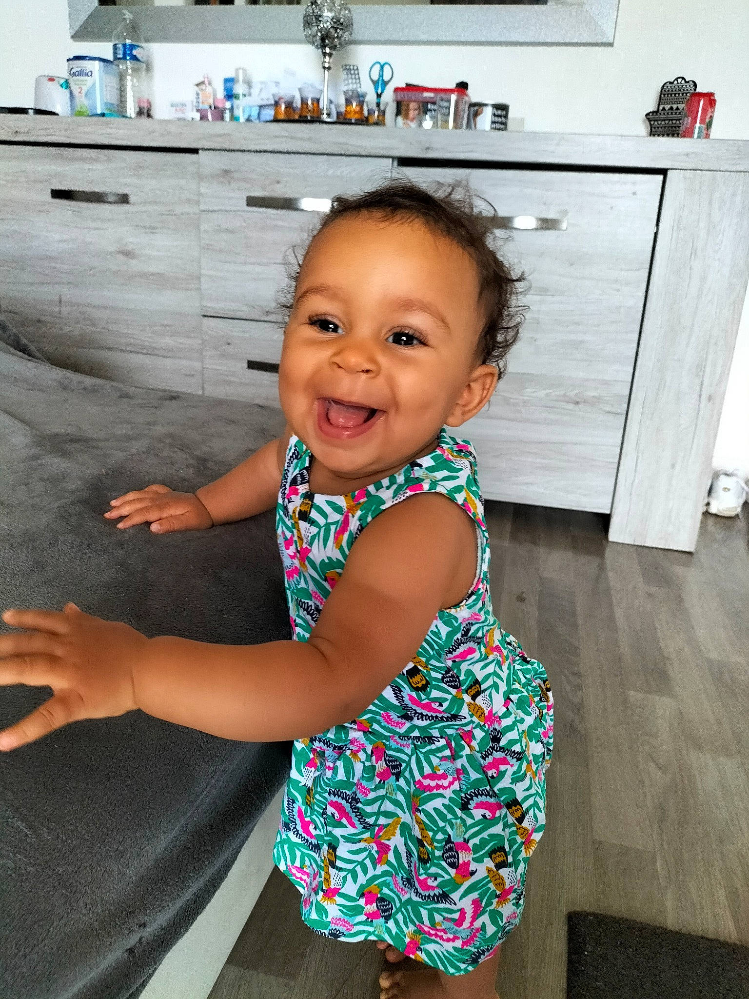 Ayana participe au concours pour gagner de l'argent avec cette photo : baby_toddler_clothing, cabinetry, child, countertop, drawer, dress, face, facial_expression, hand, happy, head, home_appliance, human_body, joy, kitchen, kitchen_appliance, kitchen_stove, leg, person, smile