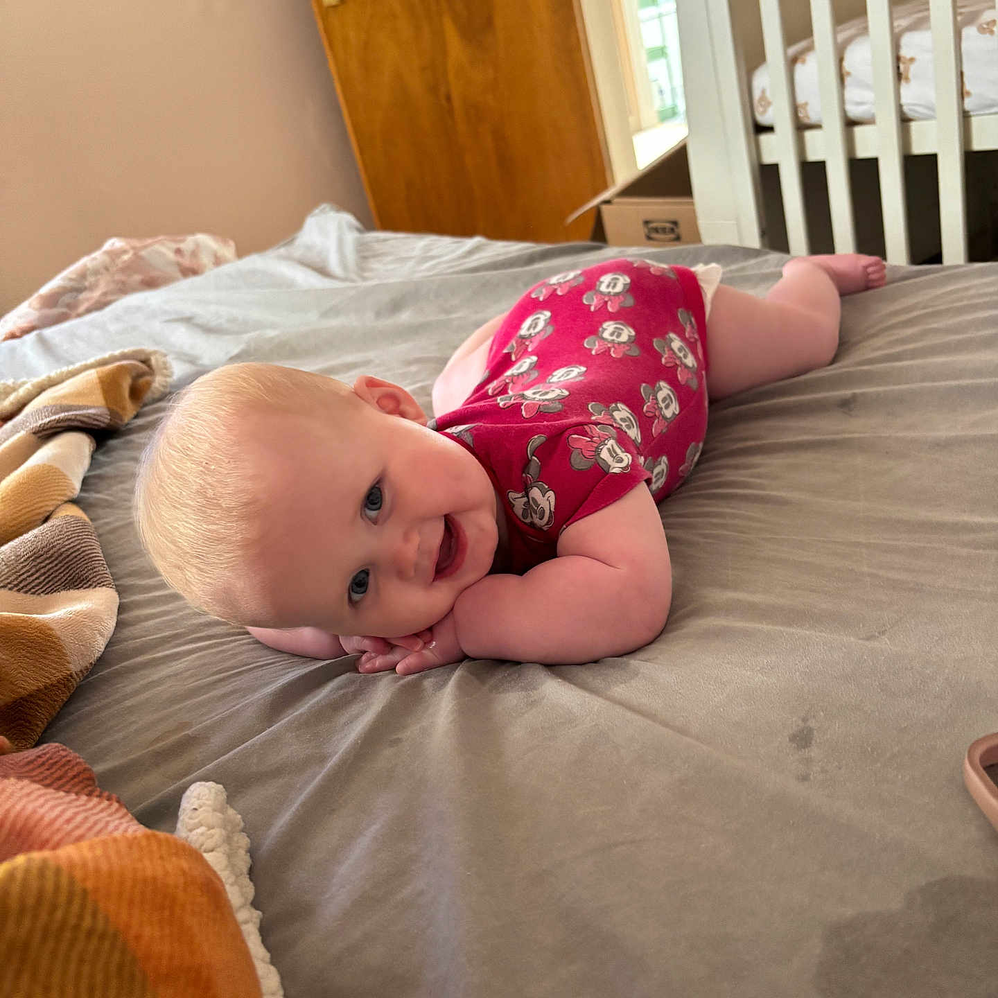 Willow joined the competition — help win amazing prizes! baby, bed, bedroom, blanket, blue_eyes, child, clothing, crib, cute, face, happy, indoor, infant, onesie, person, skin, smiling, soft, tummy, wooden_door