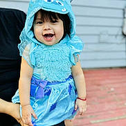 Daleyza is registered to the contest to win money with this photo: toddler, child, smiling, costume, blue, hood, monster, cute, happy, outdoor, person, face, clothing, dress, horns, hand, legs, background, wooden_deck, home