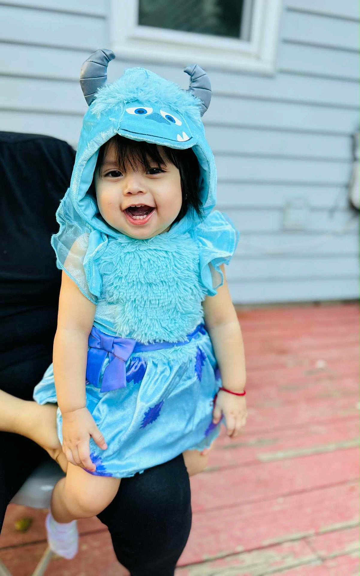Daleyza is registered to the contest to win money with this photo: toddler, child, smiling, costume, blue, hood, monster, cute, happy, outdoor, person, face, clothing, dress, horns, hand, legs, background, wooden_deck, home