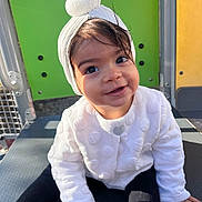 Amira a rejoint le concours — aidez-le/la à gagner de superbes lots ! toddler, child, smiling, white_jacket, headband, outdoor, playground, colorful_background, happy, cute, portrait, baby, sitting, face, person, clothing, headwear, black_pants, daylight, young_child