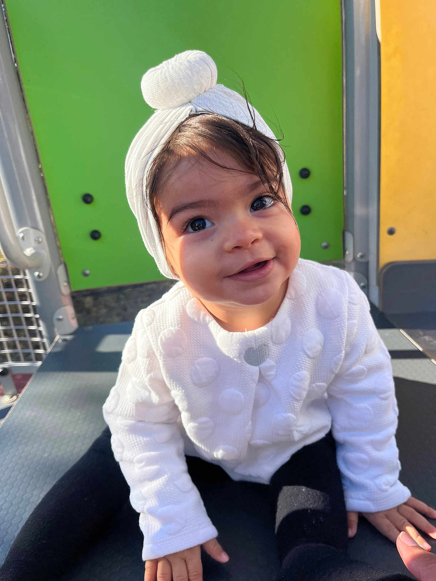 Amira a rejoint le concours — aidez-le/la à gagner de superbes lots ! toddler, child, smiling, white_jacket, headband, outdoor, playground, colorful_background, happy, cute, portrait, baby, sitting, face, person, clothing, headwear, black_pants, daylight, young_child