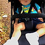 toddler, stroller, sleeping, child, blue_shirt, white_shoes, outdoor, autumn, leaves, pavement, baby, person, footwear, sitting, relaxed, daylight, casual_clothing, seat, resting, nature