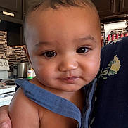Messiah is registered to the contest to win money with this photo: baby, child, face, portrait, close_up, indoor, kitchen, person, skin, expression, clothing, hand, curly_hair, cute, infant, young_child, holding, warm_lighting, domestic, casual