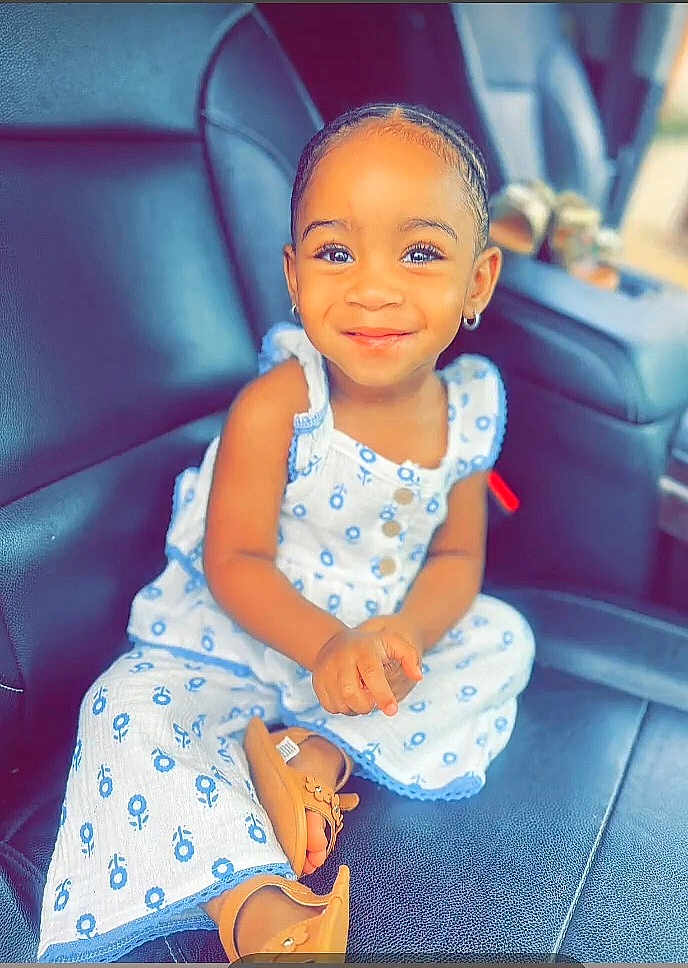 Camille joined the competition — help win amazing prizes! child, toddler, smiling, braided_hair, earrings, white_outfit, blue_flower_pattern, sitting, car_seat, leather_seat, footwear, sandals, portrait, indoor, happy, cute, young_child, person, fashion, casual
