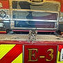kitten, cat, fire_truck, vehicle, bumper, red, yellow, metal, grill, license_plate, animal, pet, indoor, curious, small, cute, front_view, striped, ears, floor