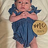 baby, infant, child, portrait, lying_down, blue_outfit, bow, headband, blanket, milestone, one_month, wooden_sign, wide_eyed, hands_clasped, bare_feet, indoor, soft_lighting, centered_composition, newborn, photography