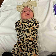 Presley is registered to the contest to win money with this photo: baby, infant, leopard_print, onesie, headband, bow, blanket, white, sleepwear, cute, lying_down, face, expression, newborn, child, clothing, soft, indoor, person, portrait