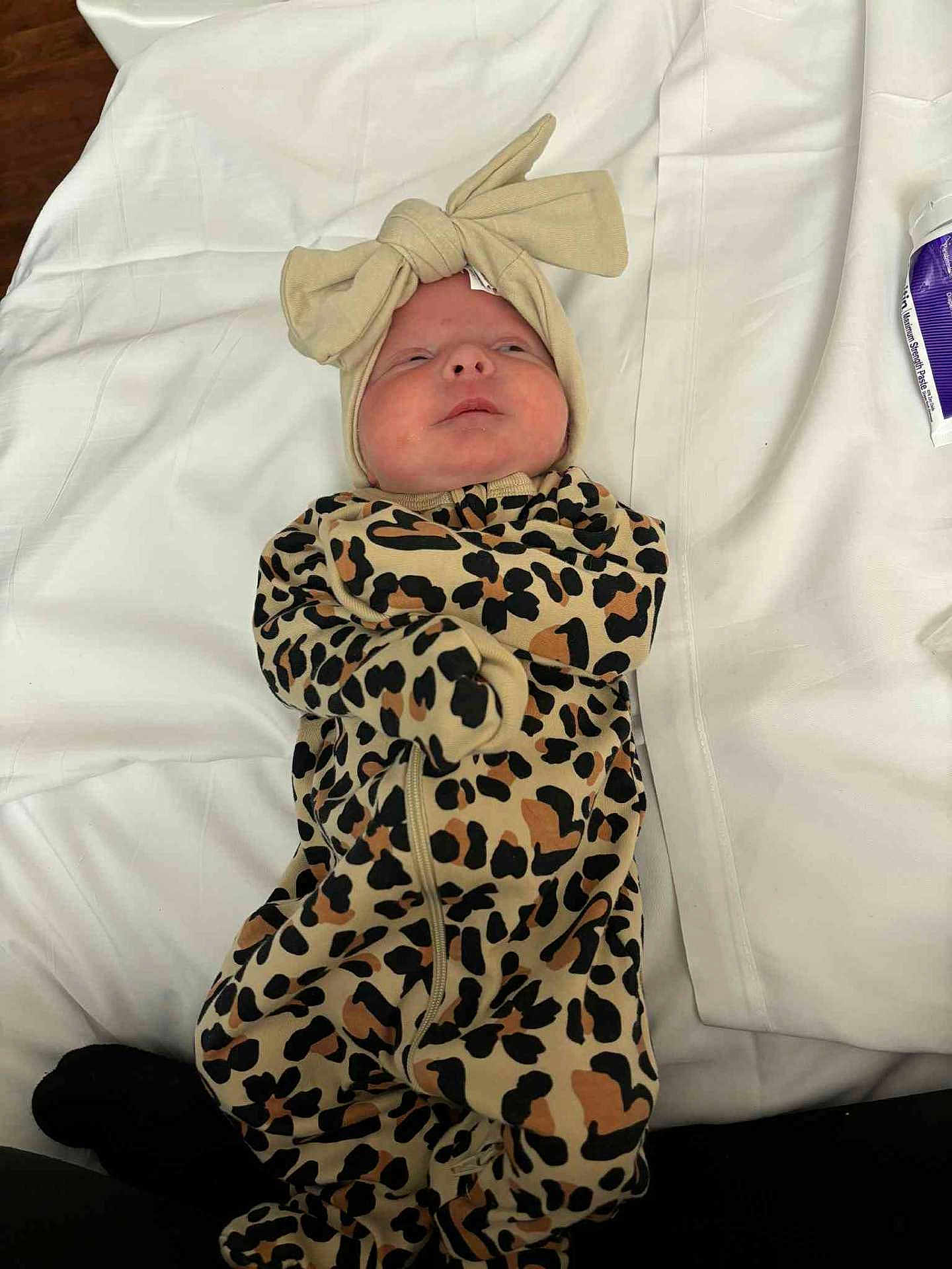 Presley is registered to the contest to win money with this photo: baby, infant, leopard_print, onesie, headband, bow, blanket, white, sleepwear, cute, lying_down, face, expression, newborn, child, clothing, soft, indoor, person, portrait