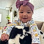 baby, smiling, headband, purple, floral_clothing, blanket, black_and_white, indoor, living_room, couch, window_blinds, child, cute, happy, portrait, furniture, hand, soft_texture, cozy, home