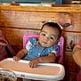 baby, child, high_chair, pink, blue_dress, bow, white, wooden_wall, table, drink, cup, indoor, person, hand, face, cute, sitting, curious, clothing, infant