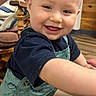 baby, child, toddler, smiling, happy, portrait, indoor, dinosaur_overalls, clothing, face, person, sitting, standing, wooden_floor, chair, furniture, home, playful, close_up, photography