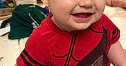 Isaiah is registered to the contest to win money with this photo: baby, black_shorts, child, face, happy, home, indoor, infant, photography, play_mat, playroom, portrait, red_shirt, short_hair, sitting, smiling, superhero_shirt, toy_cars, toys, wooden_floor