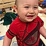 Isaiah is registered to the contest to win money with this photo: baby, child, smiling, happy, portrait, indoor, playroom, red_shirt, superhero_shirt, black_shorts, sitting, toys, toy_cars, play_mat, wooden_floor, home, face, short_hair, infant, photography