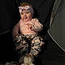 Willow joined the competition — help win amazing prizes! baby, child, infant, headband, pink_clothing, camouflage_pants, sitting, indoor, dark_background, fabric_chair, cute_expression, animal, dog, soft_lighting, portrait, playful, cozy, young_child, person, smiling