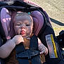 Willow is registered to the contest to win money with this photo: baby, child, car_seat, safety_harness, pigtails, tongue_out, outdoor, sunlight, shadow, seat, pink, black, clothing, infant, person, cute, expression, straps, warning_label, closeup