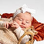 baby, infant, newborn, sleeping, headband, bow, sparkly_dress, gold_dress, basket, wicker, blanket, plush, rust_blanket, studio_shot, white_background, portrait, hands, closeup, peaceful, cute