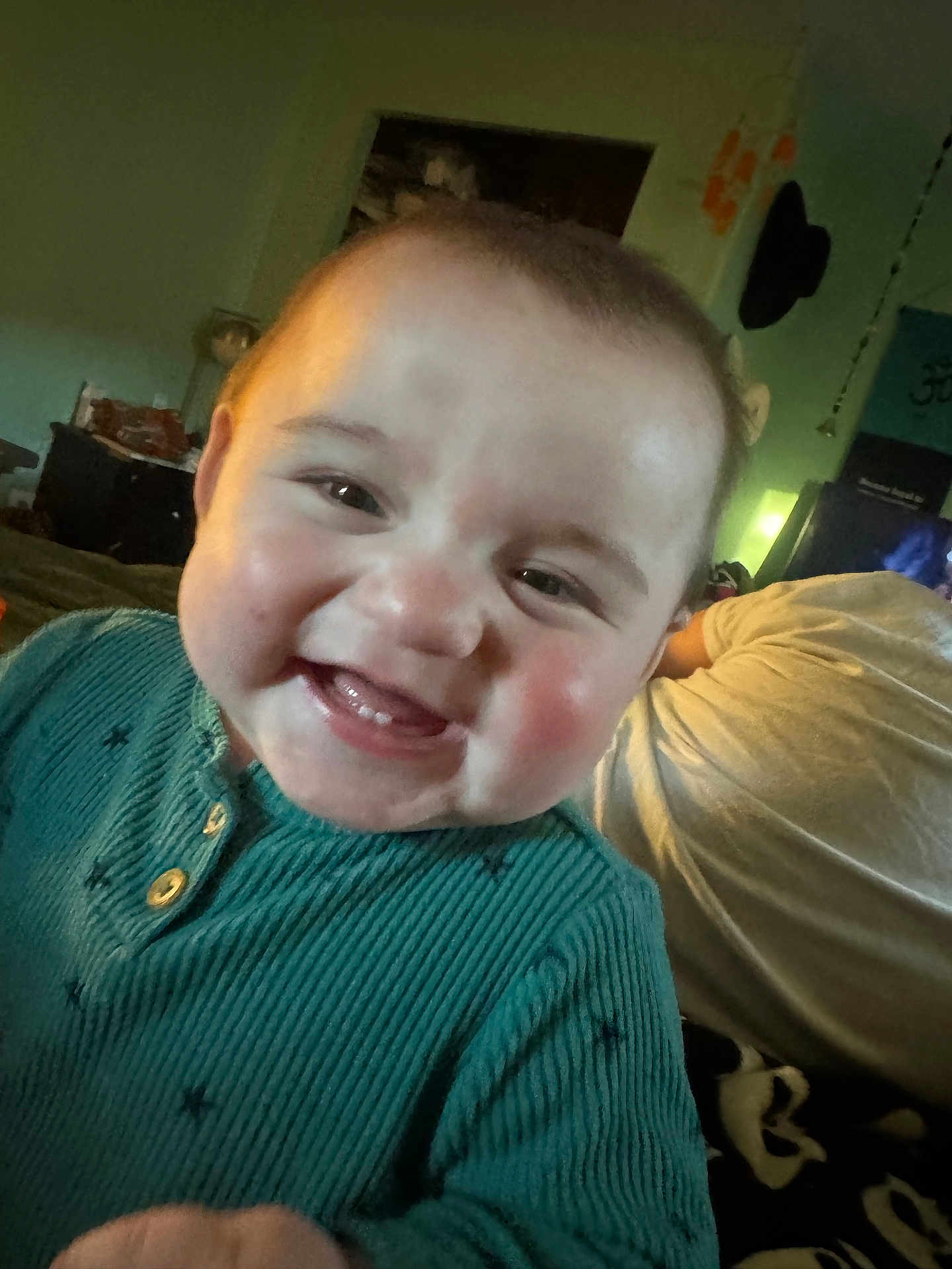 Stetson joined the competition — help win amazing prizes! baby, infant, smiling, teeth, rosy_cheeks, closeup, portrait, teal_sweater, ribbed_sweater, indoor, bedroom, blanket, adult_in_background, face, eyes, cheeks, mouth, happy, candid, toddler