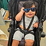 Rudy joined the competition — help win amazing prizes! baby, child, sunglasses, stroller, smile, gray_outfit, cute, indoors, seatbelt, happy, chubby, shorts, shirt, black_hair, person, toddler, fashion, casual, fun, portrait