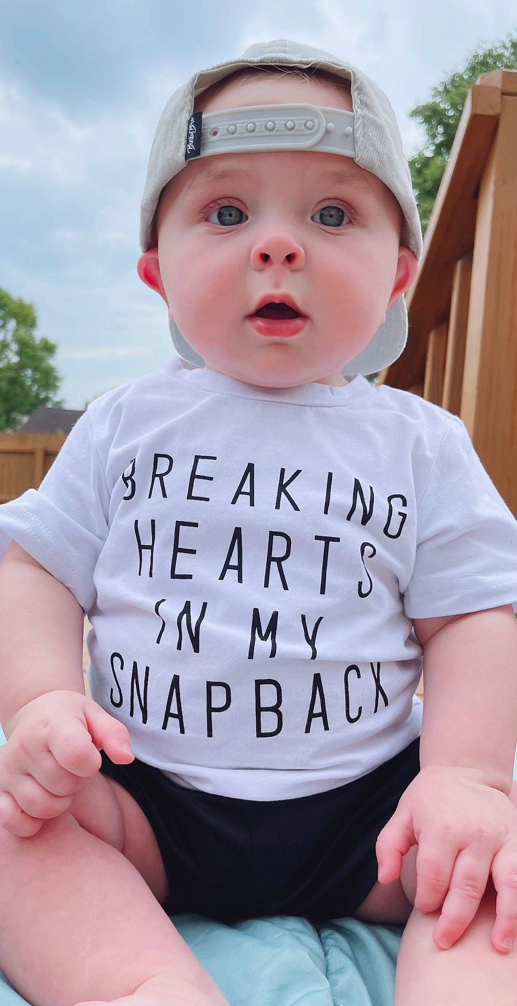 Cade is registered to the contest to win money with this photo: baby, baby_toddler_clothing, cap, child, cool, eye, finger, gesture, grass, happy, headwear, person, photograph, pink, recreation, sitting, sky, sleeve, surprise, t_shirt