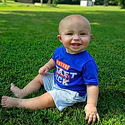 Halo is registered to the contest to win money with this photo: baby, child, grass, outdoor, smiling, happy, blue_shirt, shorts, sitting, nature, greenery, sunlight, portrait, cute, one_person, infant, playful, daytime, casual_clothing, grass_field