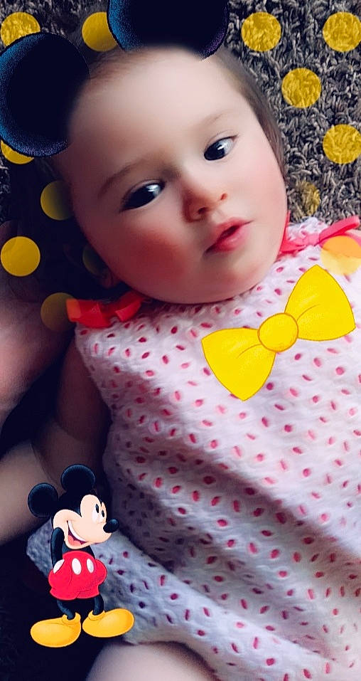 Gabriella is registered to the contest to win money with this photo: baby_toddler_clothing, cheek, doll, eyelash, facial_expression, happy, lip, mammal, organ, pattern, people, person, pink, product, red, skin, sleeve, textile, toddler, toy