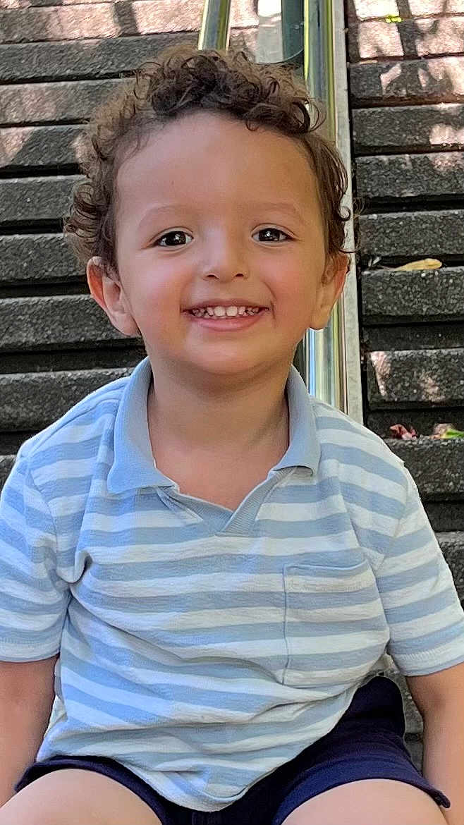 Haron participe au concours pour gagner de l'argent avec cette photo : child, toddler, smiling, curly_hair, striped_shirt, polo_shirt, shorts, outdoor, stairs, daylight, happy, sitting, face, skin, person, casual_clothing, young_child, cute, portrait, playful