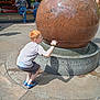 Truman is registered to the contest to win money with this photo: child, boy, red_hair, granite_sphere, outdoor, playful, shadow, pumpkins, festival_booth, casual_clothing, sandals, crouching, concrete, summer, daylight, people, background, fun, curiosity, public_place