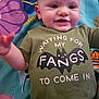 baby, child, smiling, green_shirt, bat_graphic, text_on_clothing, play_mat, colorful_background, infant, cute, lying_down, happy, person, face, head, eyes, mouth, arm, hand, toddler