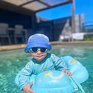 Farell a rejoint le concours — aidez-le/la à gagner de superbes lots ! toddler, child, pool, water, float, inflatable_ring, sunglasses, hat, blue, sunny, outdoor, summer, water_toys, baby, swimming, playful, daylight, fun, relaxation, vacation