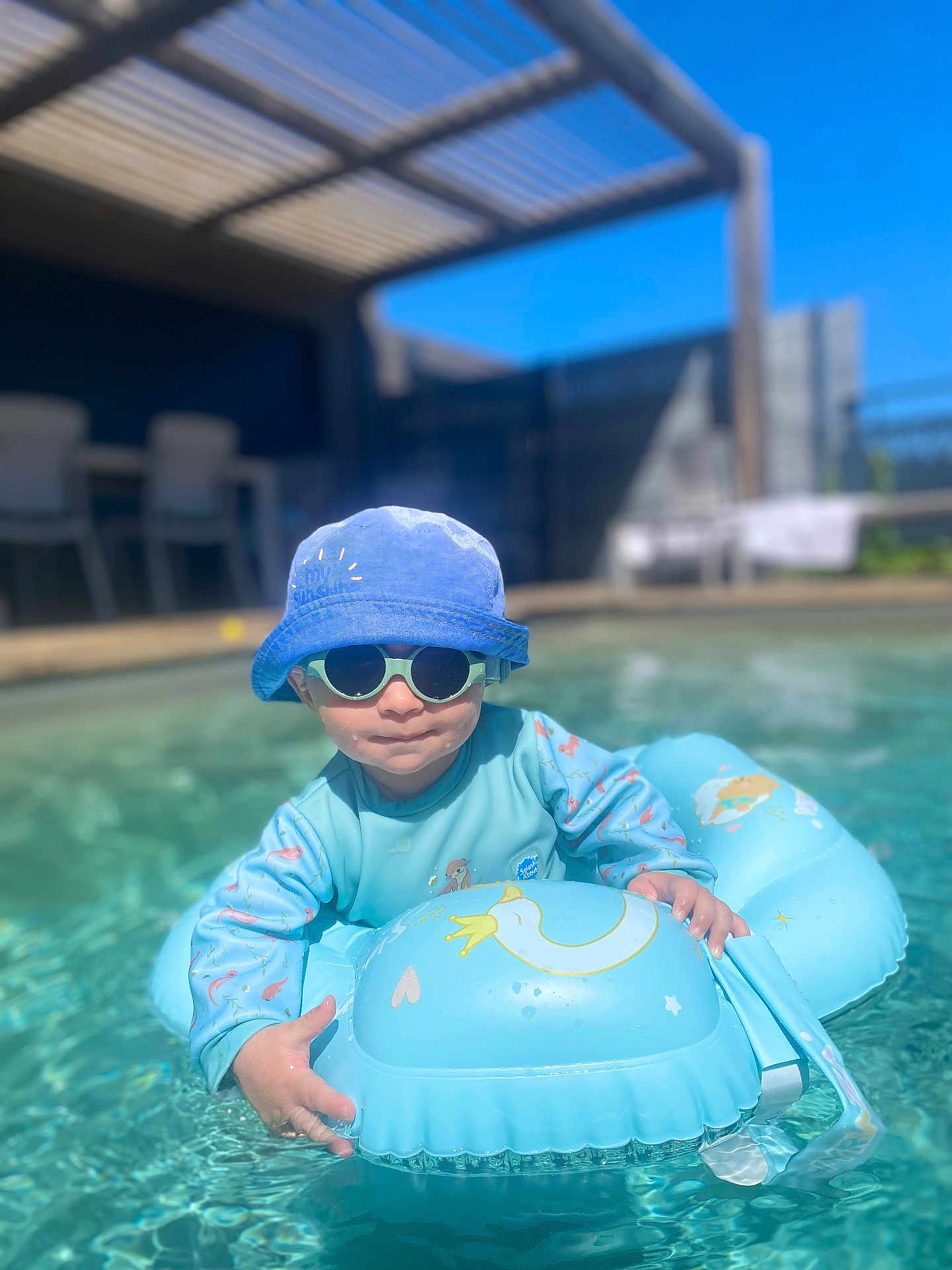 Farell a rejoint le concours — aidez-le/la à gagner de superbes lots ! toddler, child, pool, water, float, inflatable_ring, sunglasses, hat, blue, sunny, outdoor, summer, water_toys, baby, swimming, playful, daylight, fun, relaxation, vacation